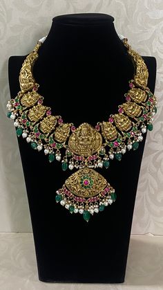 The Antique Kundan Lakshmi Necklace is a masterpiece of traditional Indian craftsmanship, representing the regal heritage of temple jewelry. At its centerpiece, it features a finely detailed depiction of Goddess Lakshmi, the Hindu goddess of wealth and prosperity, intricately carved in gold. Surrounding the central deity are vibrant, hand-set Kundan gemstones—emeralds, rubies, and diamonds—arranged in floral and geometric patterns. The necklace is designed with each element embossed with antique Luxury Meenakari Temple Necklace For Diwali, Temple Necklace, Goddess Of Wealth, Hindu Goddess, Temple Jewelry, Wealth And Prosperity, Indian Necklace, The Hindu, Golden Jewelry