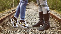 two people standing on train tracks wearing black and white shoes