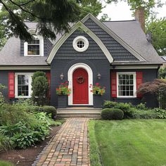 a blue house with red shutters on the front door and brick walkway leading to it