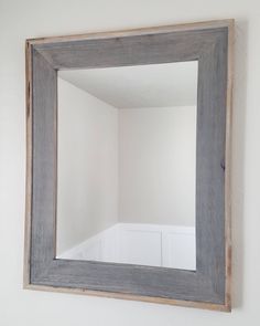 a mirror hanging on the wall above a sink in a room with white walls and wood trim