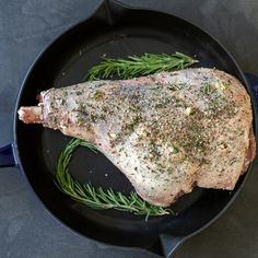 a piece of meat in a skillet with rosemary sprigs on the side