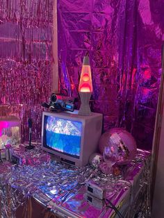 a table topped with a tv sitting next to a purple wall covered in tinsel