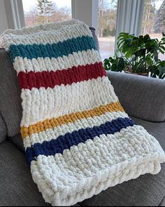 a crocheted blanket sitting on top of a couch next to a potted plant