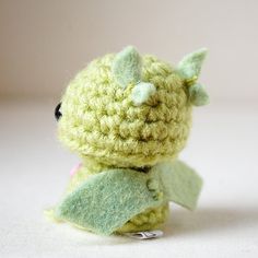 a small green crocheted stuffed animal sitting on top of a table next to a white wall