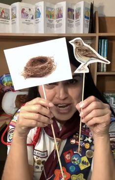 the woman is holding up two birds on sticks with stickers in front of her face