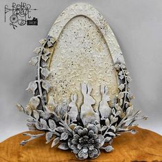 an ornately decorated egg on top of a wooden stand with silver flowers and leaves