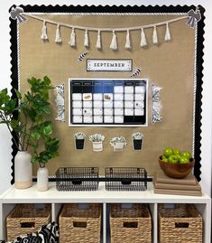 a white table topped with baskets filled with fruit and veggies next to a wall calendar