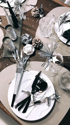 the table is set with black and white plates, silver utensils and pine cone centerpieces