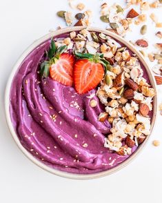 a bowl filled with fruit and nuts on top of a white table next to a spoon