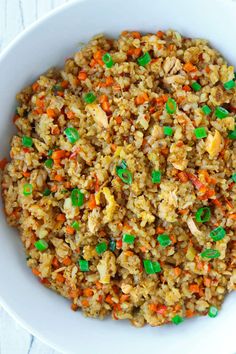 a white bowl filled with fried rice and carrots, topped with green peas on the side