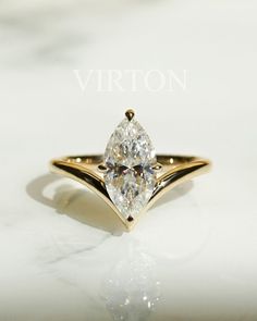 a yellow gold ring with a pear shaped diamond on it's side, sitting on a white surface