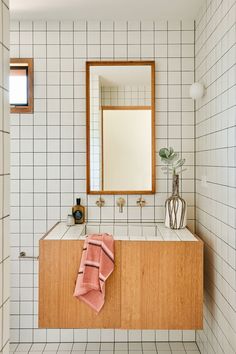 a white tiled bathroom with a wooden cabinet and mirror above the sink, along with a pink towel on the counter