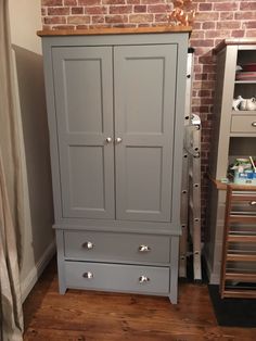 a grey armoire with drawers in front of a brick wall and wooden flooring