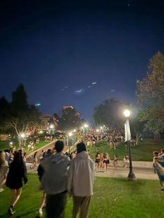 many people are walking around in the park at night, some have their lights on