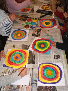 children are painting circles on paper with paintbrushes at a table that is covered in newspaper