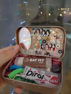 someone is holding an open tin box with various items inside