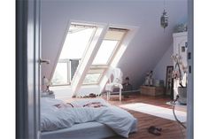 an attic bedroom with slanted windows and white bedding, hardwood floors, and wooden flooring