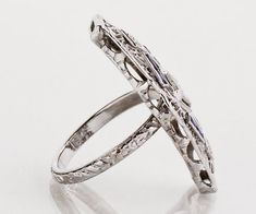 This unique one-of-a-kind antique conversion has been created out of the center of a 1920's filigree diamond and sapphire bracelet and a 1920's original etched wedding band. A fantastic Art Deco gift if we do say so ourselves!! Antique Ring - Antique Art Deco 18k White Gold Filigree Sapphire and Diamond Conversion RingArt Deco18k White GoldConversion3 Diamonds =.10ct8 French Cut Sapphires =.15ctRing Size Approximately 5.5 - 6. See photos of curve on center section. Ring measures 2.25" in length Victorian Engraved Ring With Polished Finish For Wedding, Antique Collectible Platinum Ring, Victorian White Gold Rings With Polished Finish, Victorian Style Polished White Gold Ring, Victorian Platinum Filigree Jewelry, Art Deco Sterling Silver Filigree Ring With Diamond Cut, Vintage Filigree Ring With Decorative Band, Art Deco Filigree Ring For Promise, Ornate Platinum Jewelry