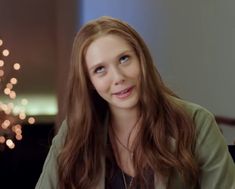 a woman with long red hair sitting in front of a firework display and looking at the camera