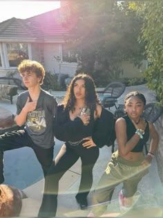 three young people posing for the camera in front of a house with a swimming pool