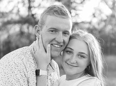 black and white photograph of a man and woman smiling at the camera with trees in the background