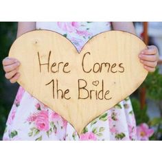 a wooden sign that says here comes the bride in front of a woman holding a heart