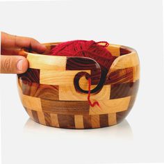 a hand is knitting yarn in a wooden bowl