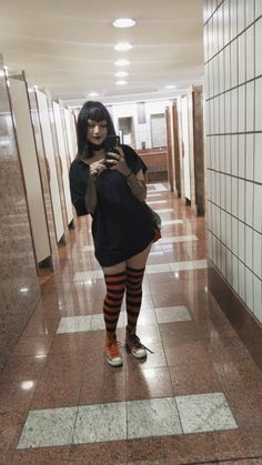 a woman in black dress and striped socks standing on tiled floor looking at her cell phone