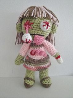 a crocheted zombie doll is posed on a white surface, wearing a pink and brown dress