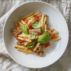 a white bowl filled with pasta and meat on top of a striped cloth next to a fork