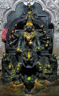 an idol is displayed in front of a silver statue with yellow decorations on the face