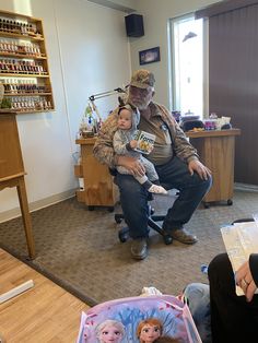 an older man sitting in a chair holding a baby while another person sits on the floor