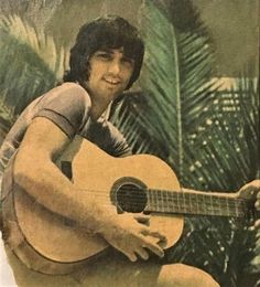 an old photo of a man holding a guitar in front of palm trees and plants