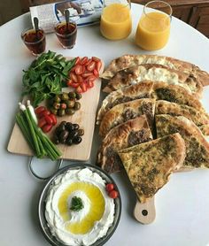 a white table topped with lots of food and veggies next to glasses of orange juice