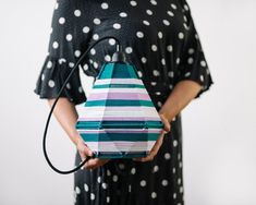 a woman in a black dress is holding a blue and pink object with white dots on it