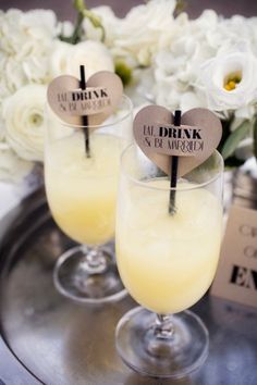 two glasses filled with drinks sitting on top of a metal tray next to white flowers