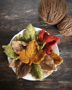 a white plate topped with crocheted leaves and balls of yarn next to it