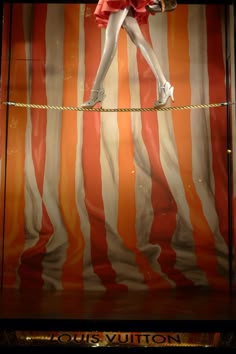 a mannequin dressed in red and white is balancing on rope with an orange striped background