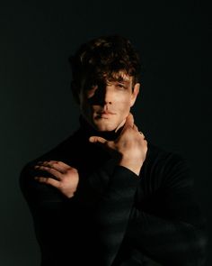 a man with his hands on his chest posing for a photo in front of a dark background