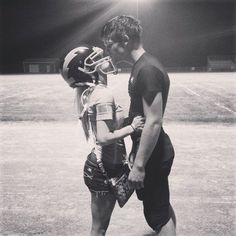 a couple of people standing next to each other on top of a field with a football helmet