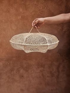 a person holding a white bird cage on top of a brown ground with dirt in the background