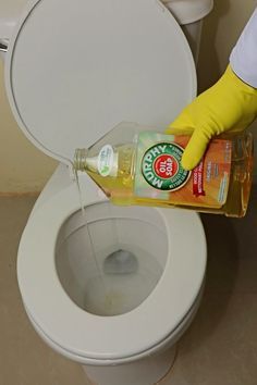 a person in yellow gloves is cleaning a toilet with a bottle of sanitizer