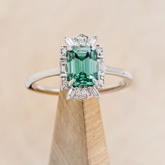 Product Details Ring Style: The "Cleopatra" is an emerald-cut green moissanite women's engagement ring with diamond accents. Many other center stone options are available upon request. Center Stone: 8x6mm Emerald-Cut Green Moissanite Materials: 14K gold engagement ring featuring a green moissanite center stone and 1/5 CTW accent diamonds Customizable: Basic customizations can be accommodated by simply adding a request in the “Custom Requests” section during checkout. A common example is to request a darker-colored stone of the same material. For more extensive customizations, such as stone swaps, please contact us! We would be honored to make your ring even more meaningful! Available In: 14K White Gold, 14K Yellow Gold, or 14K Rose Gold Dreaming Bigger? Because each ring is handcrafted to Green Moissanite Engagement Ring, Green Moissanite, Staghead Designs, Colored Stone, Ring With Diamond, Ceramic Rings, Montana Sapphire, Detailed Ring, Unisex Ring