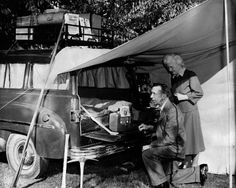 an old black and white photo of two people next to a car under a tent