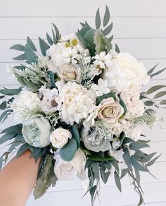 a bouquet of white flowers and greenery is being held by someone's hand