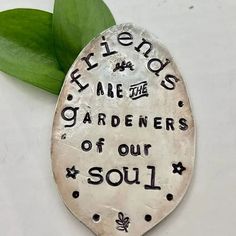 a metal spoon sitting on top of a white surface next to a green leaf and the words friends are the gardener's of our soul