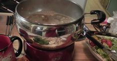 a pot full of soup sitting on top of a table next to a plate with food