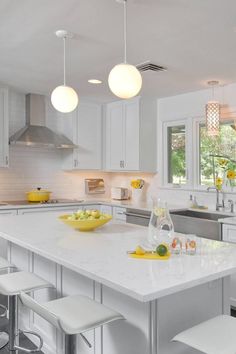 a kitchen with white cabinets and countertops has yellow dishes on the island in front of the sink