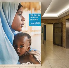 a woman holding a baby in her arms next to a large poster with the words for every child in danger