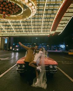 a bride and groom posing on the hood of a car in front of a carnival